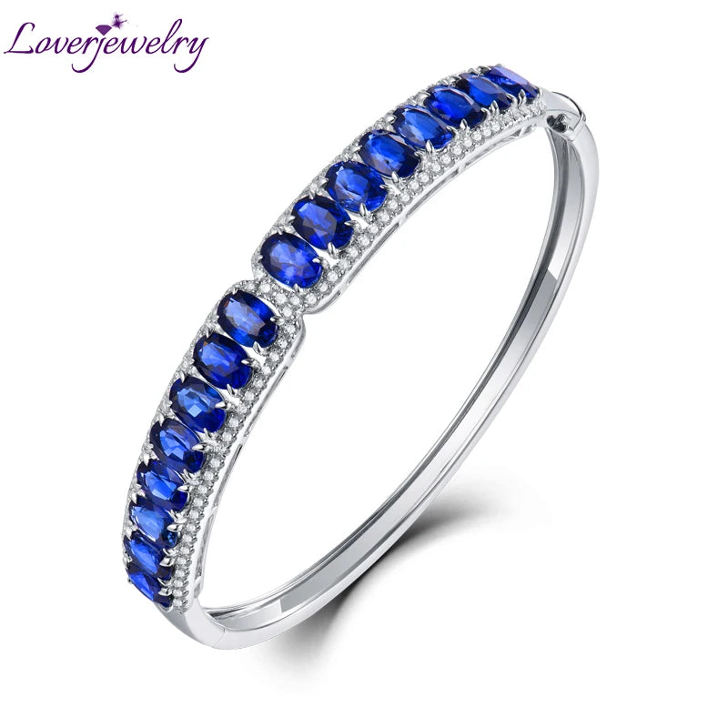 A silver bangle bracelet featuring a curved top band set with rows of oval blue gemstones and small clear accent stones, shown on a white background with the Loverjewelry logo in the top left corner.