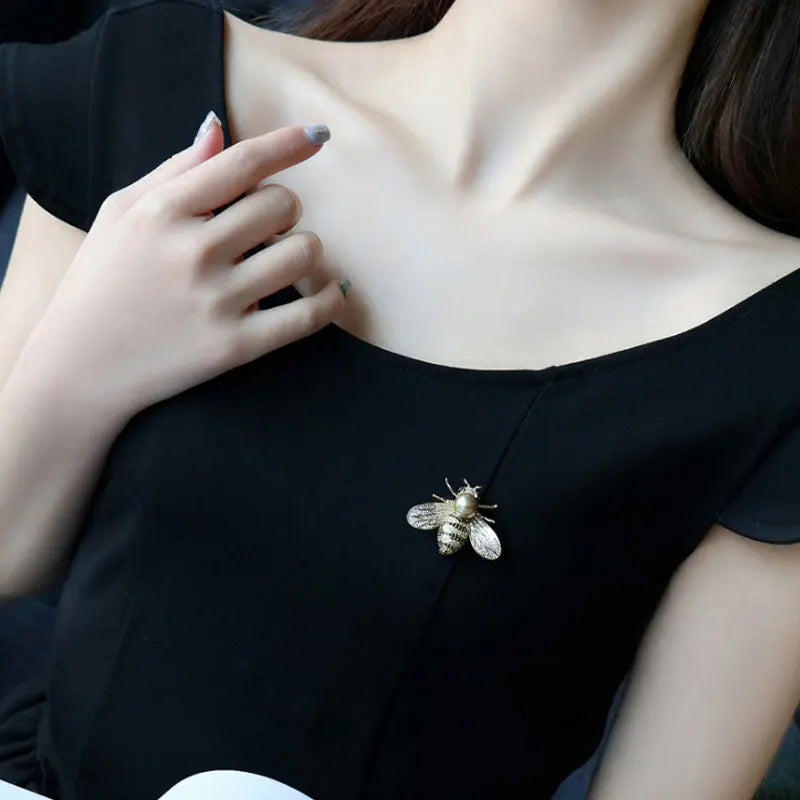 Woman wearing a black top with a bee-shaped brooch on a neutral background