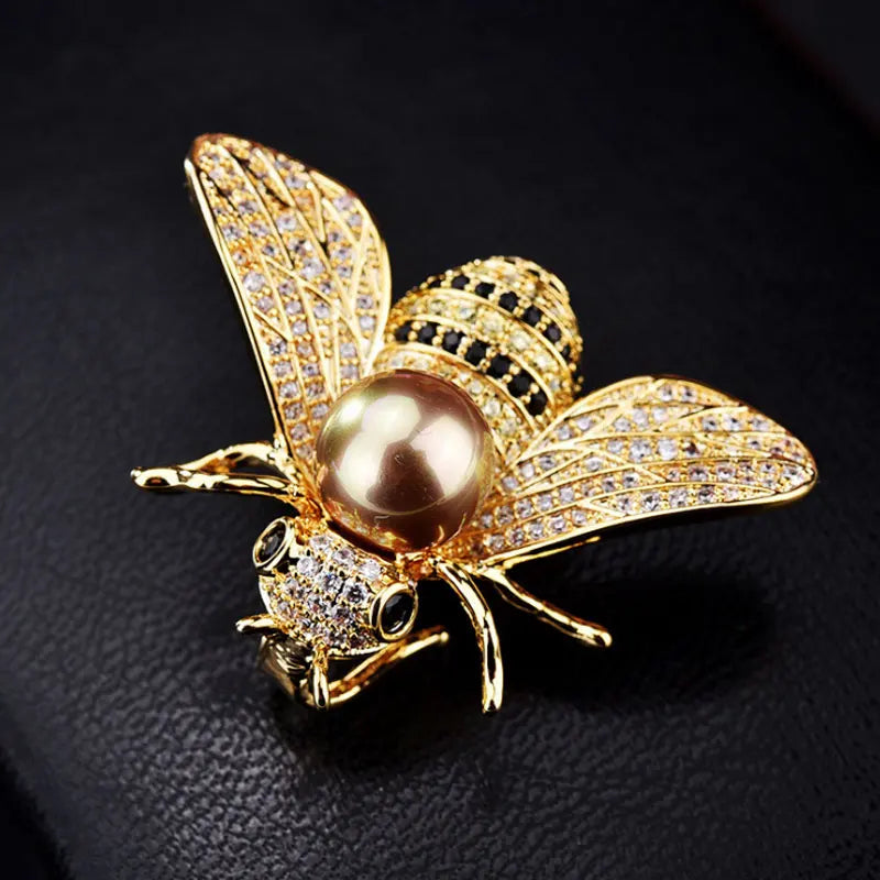 Gold bee-shaped brooch with a pearl on a dark background