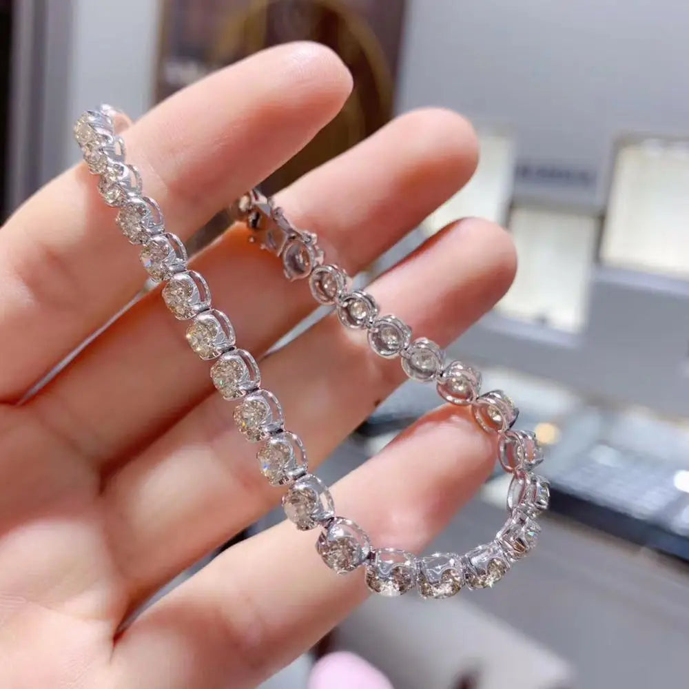 Silver bracelet with clear stones held in a hand against a blurred indoor background