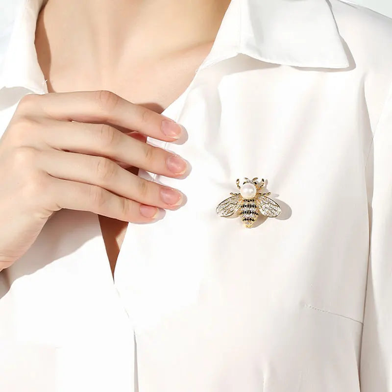 Hand wearing a white glove with a decorative bee brooch on a white shirt.