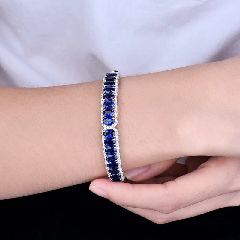 A close-up of a silver-toned bracelet with two linked sections, each set with deep blue oval gemstones and small clear accent stones, worn on a person's wrist with a hand resting below.