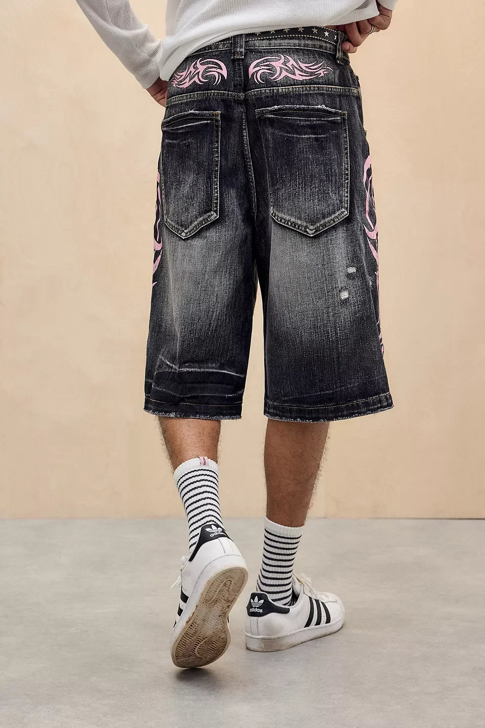 Person wearing black denim shorts with pink floral patterns on a beige background