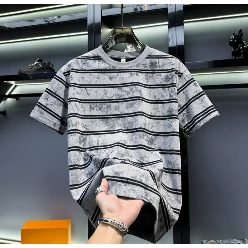 Gray and black striped t-shirt on a hanger with a hand holding it, blurred background