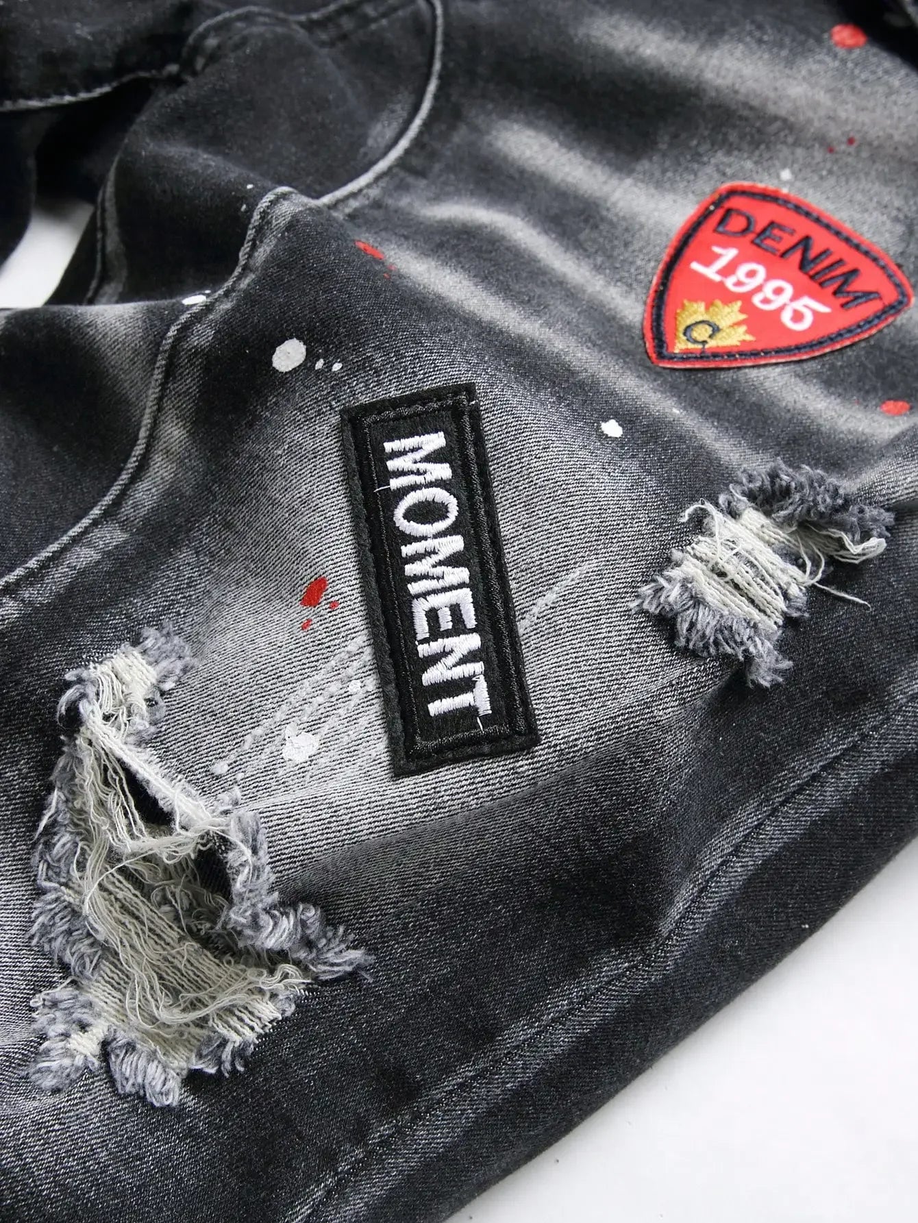 Black distressed denim jacket with 'Moment' and 'Denim 1896' patches on a white background
