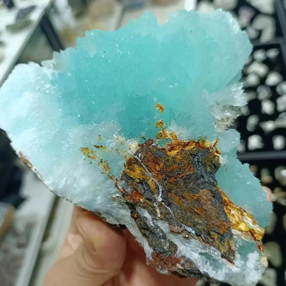 Turquoise crystal with metallic inclusions held by a hand against a blurred background