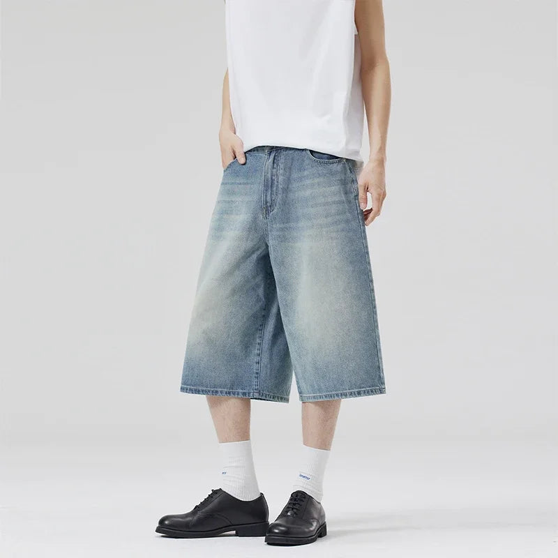 Person wearing light blue denim shorts, white shirt, black shoes, and white socks on a plain background