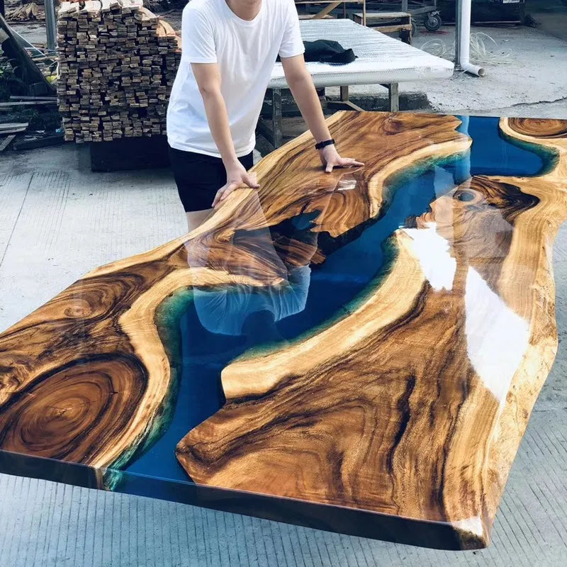 Person touching a wooden table with blue resin inlay outdoors.