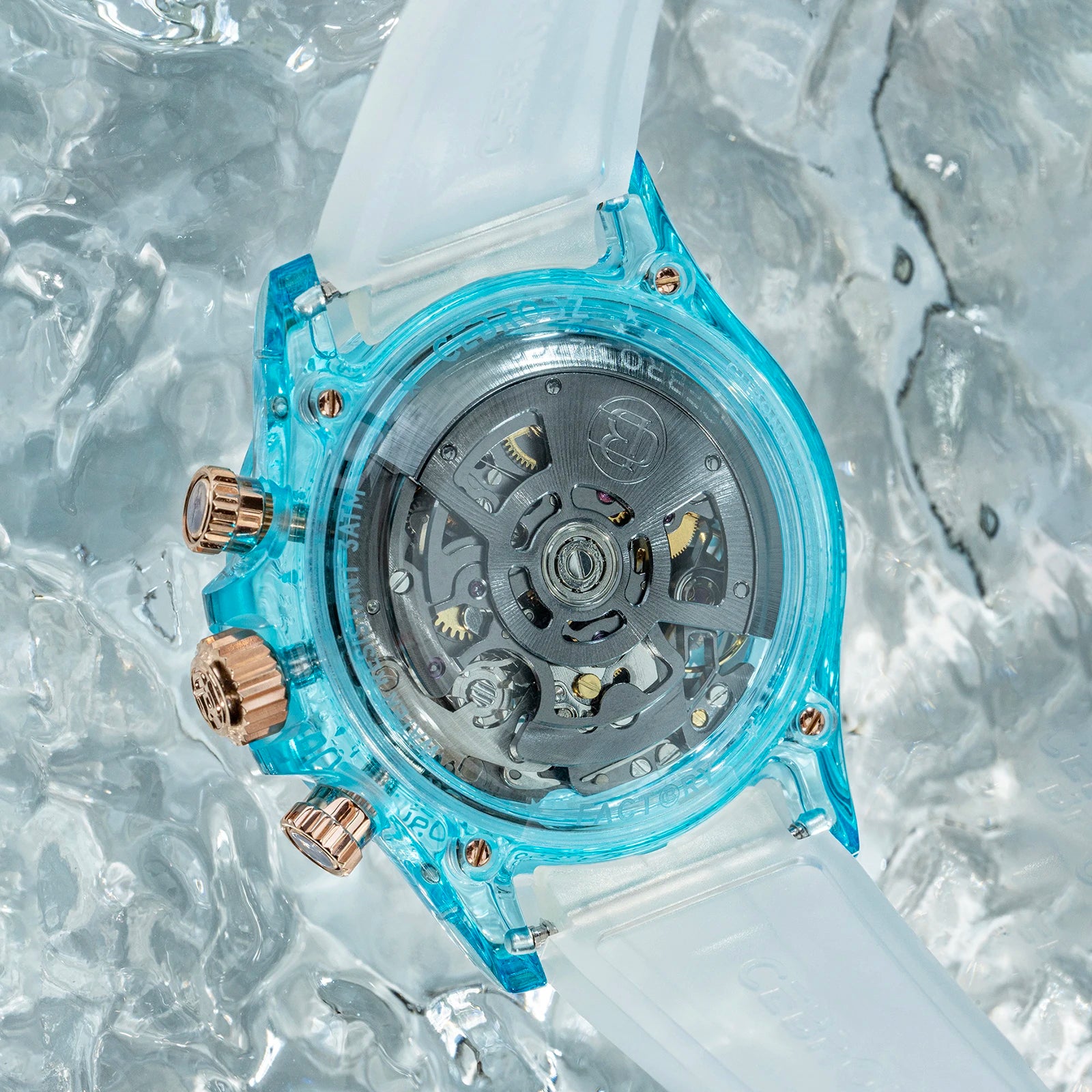 A Casio watch with a translucent light blue case and a frosted white strap, shown from the back with its mechanical movement visible. The watch has rose gold-tone chronograph buttons and is photographed on a textured, icy background.
