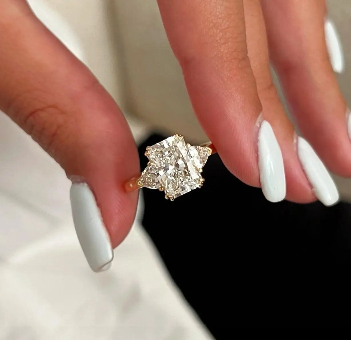 Diamond ring on a hand with white nail polish against a neutral background