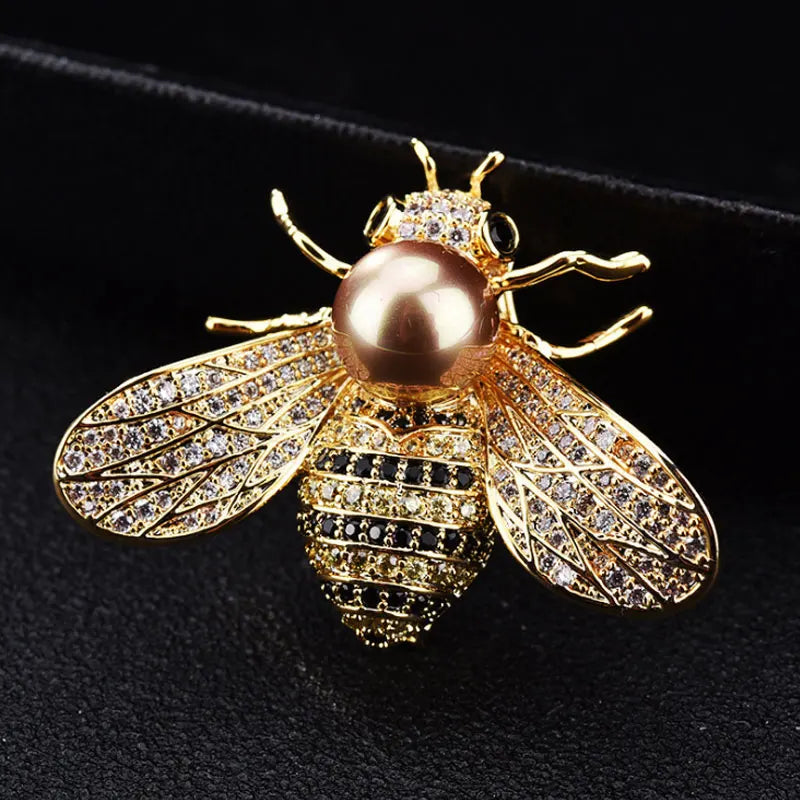 Gold bee-shaped pendant with pearl body on a black background