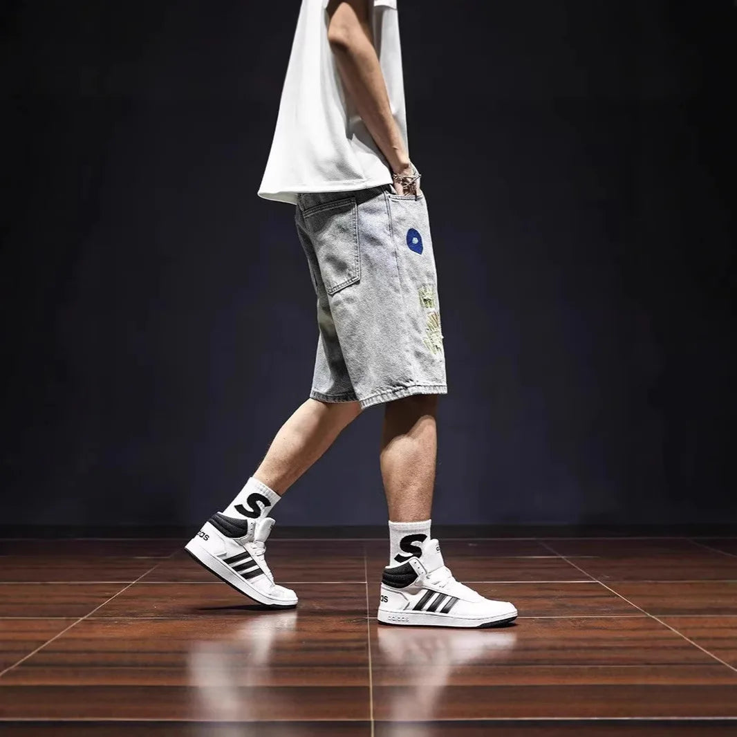 Person wearing white sneakers with black stripes, light gray shorts, and black socks with a logo on a dark background.