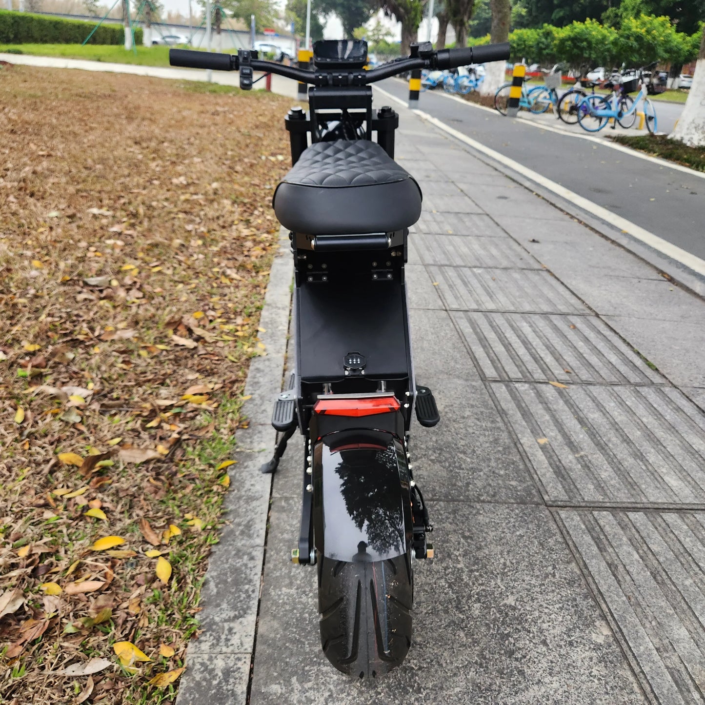 Black electric scooter on a sidewalk with a road and parked bicycles in the background