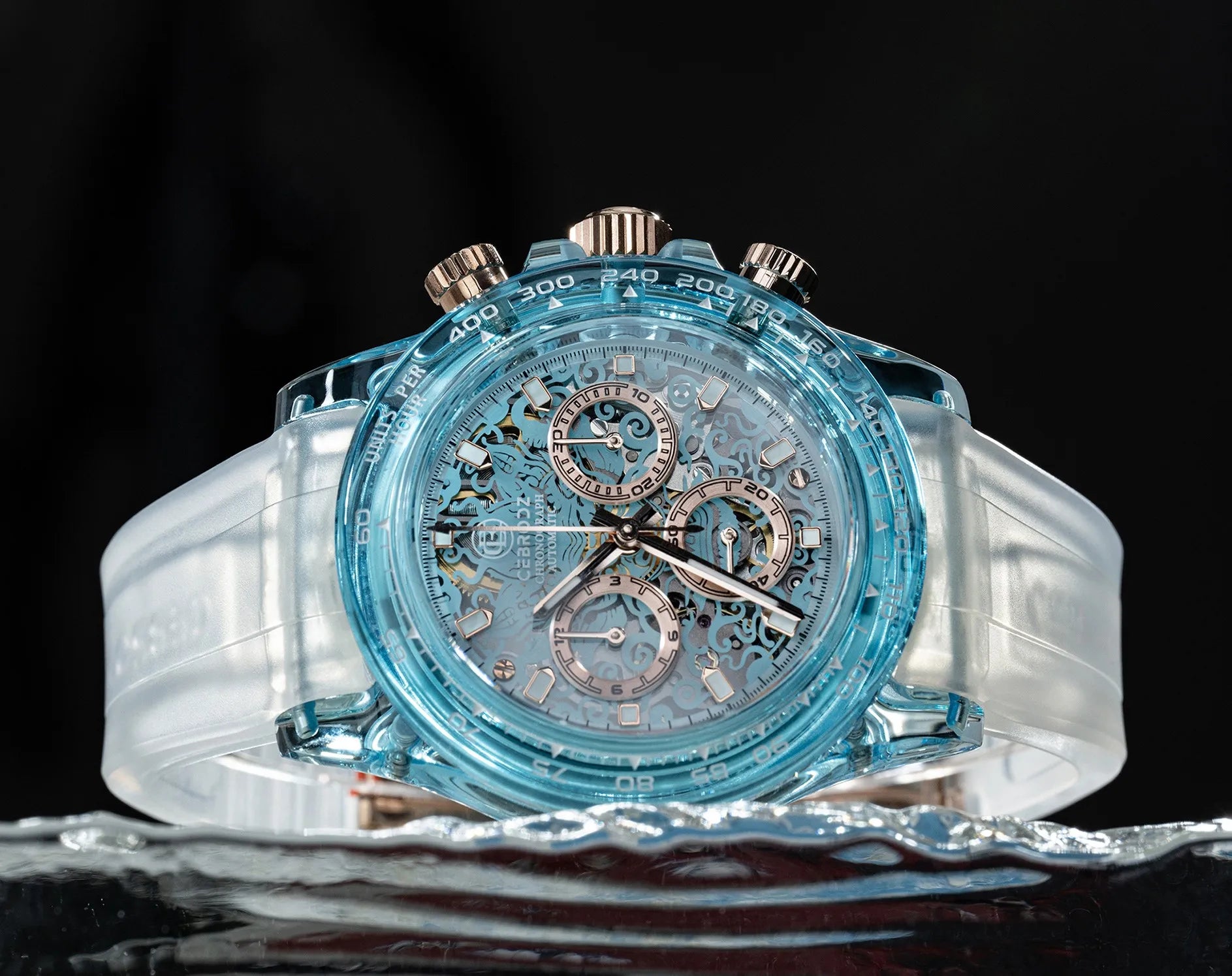 A luxury chronograph watch with a transparent light blue case, a white rubber strap, and rose gold-toned pushers and subdials, displayed on a reflective surface against a black background.