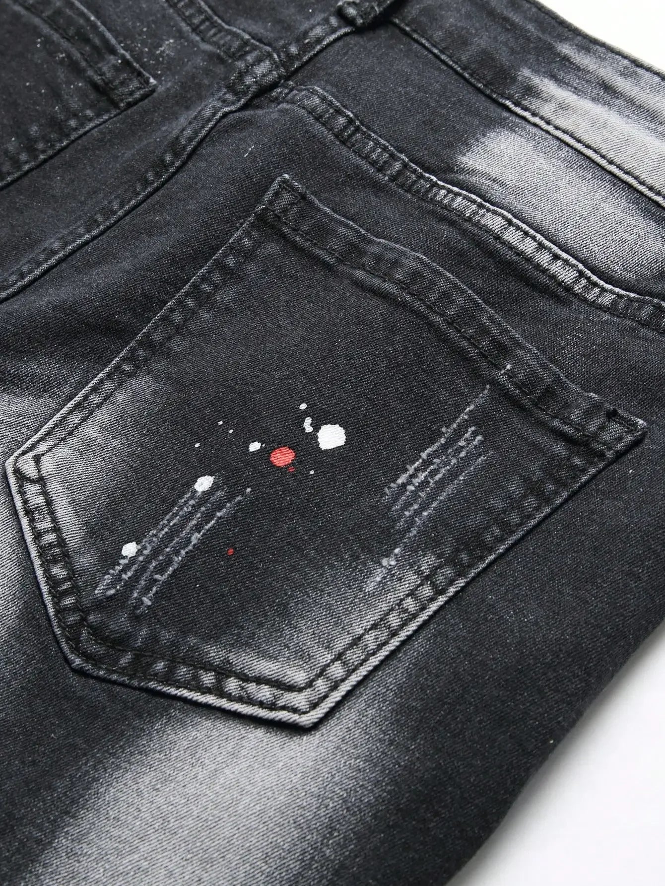 Black distressed jeans with paint splashes on a white background