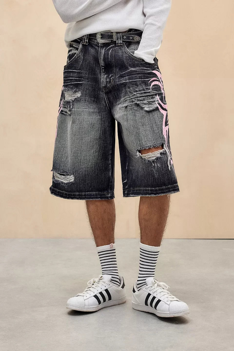 Person wearing ripped denim shorts, white sneakers with black stripes, and striped socks on a beige background