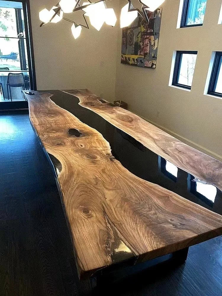 Wooden dining table with black resin finish in a room with large windows.