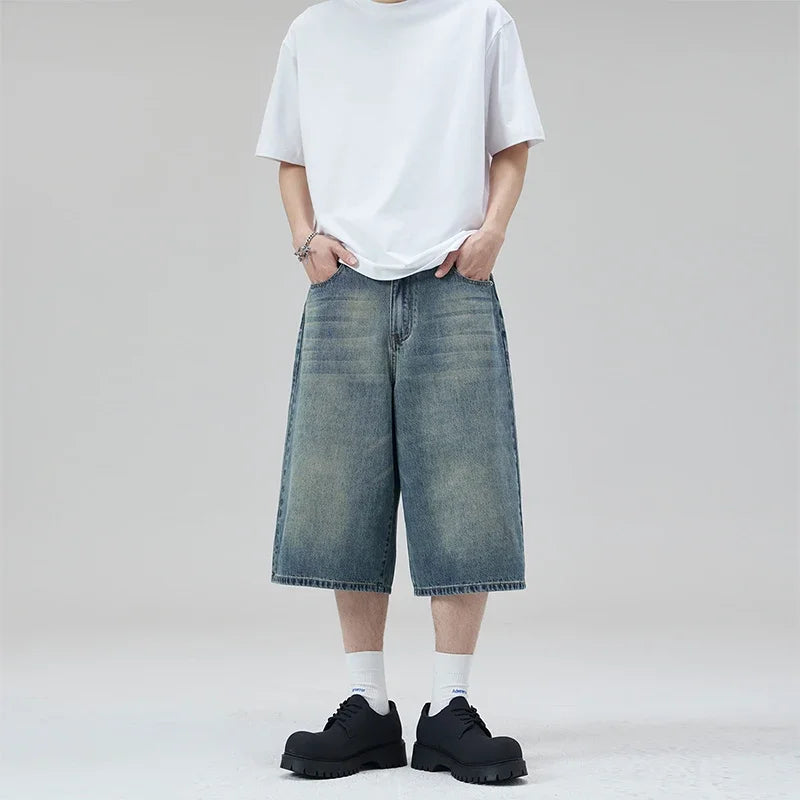 Person wearing a white t-shirt, blue denim shorts, and black shoes on a plain background