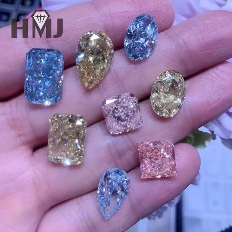 A hand holding multiple loose diamonds in different colors and shapes, including blue, yellow, and pink tones, with an HMJ logo in the top left corner.