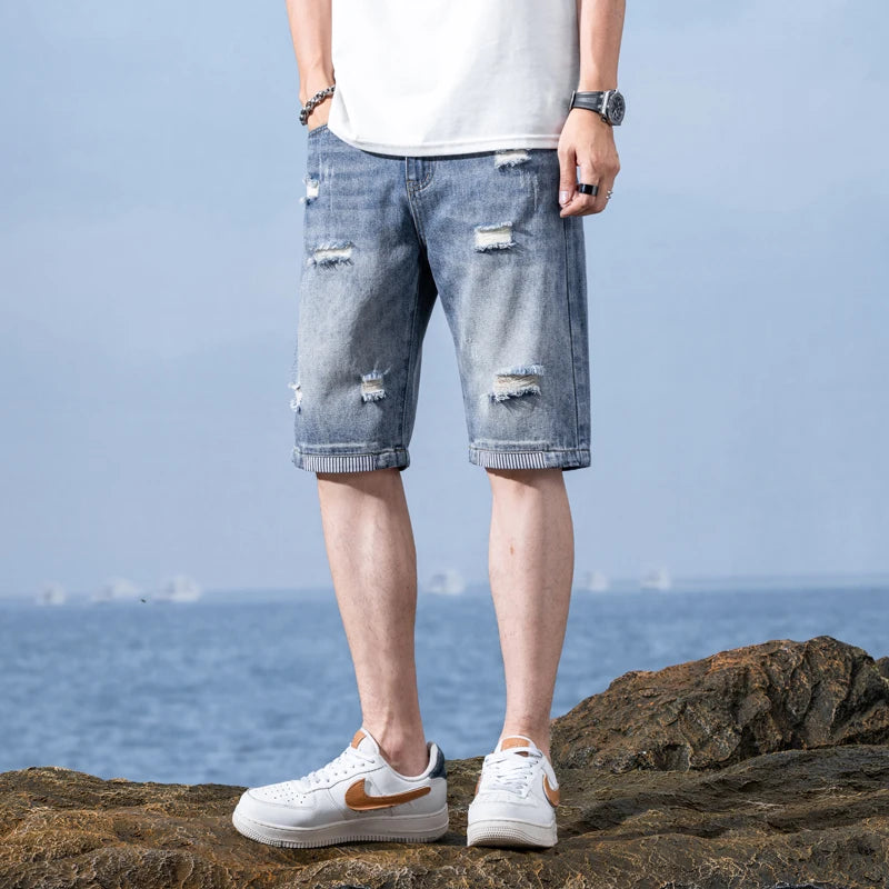 Person wearing ripped blue jeans and white sneakers on a rocky surface with a blue sky background