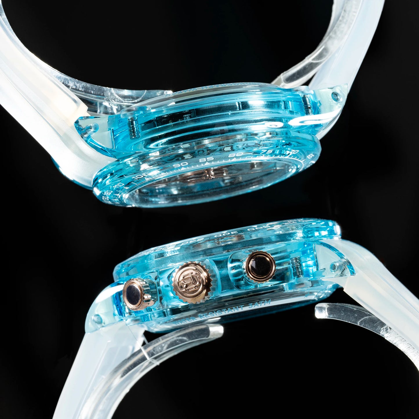 Close-up of a smartwatch with a transparent light blue case and clear strap, shown from two angles against a black background.