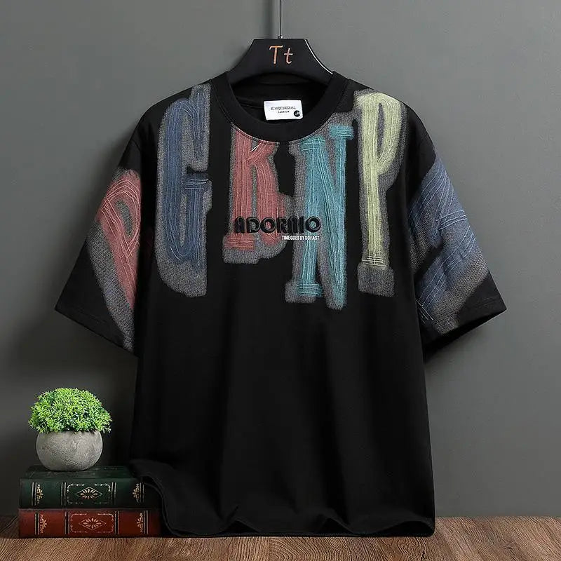 Black t-shirt with colorful text design on a hanger against a gray wall.