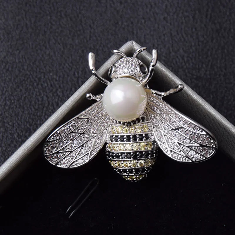 Silver bee-shaped brooch with a pearl body on a dark background