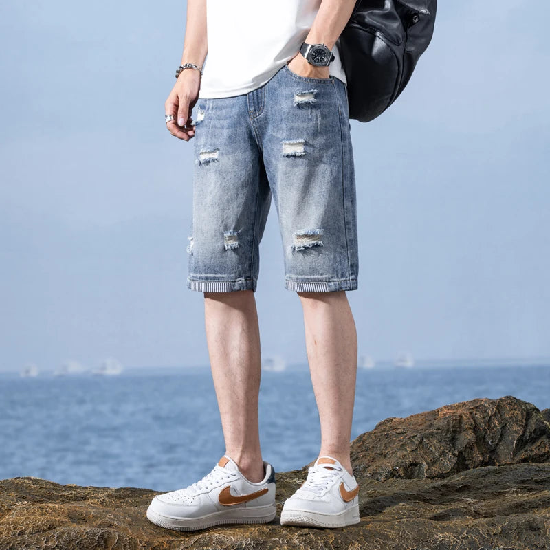 Person wearing ripped blue jeans and white sneakers standing on rocks with a clear sky background