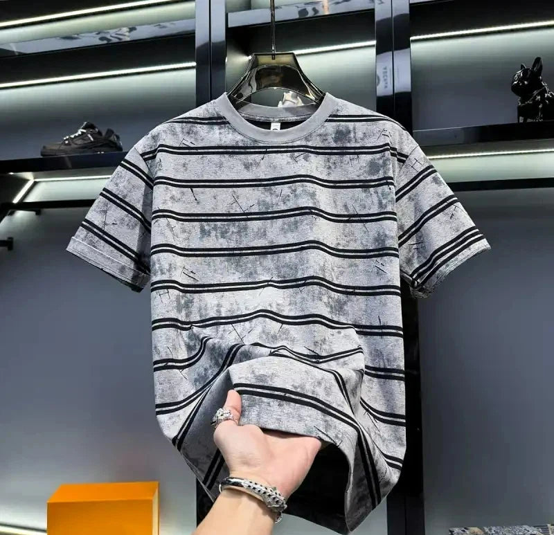 Gray and black striped t-shirt on a hanger with a hand holding it, against a dark background.