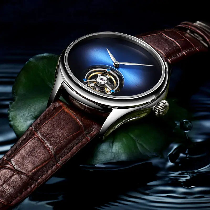 A luxury wristwatch with a blue gradient dial, a visible tourbillon movement through the lower dial, and a brown leather strap, resting on dark water with green leaves.