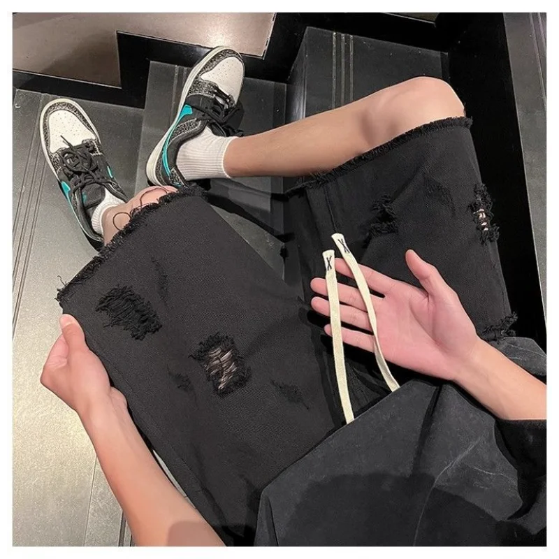 Person wearing black ripped jeans and sneakers sitting on a chair.