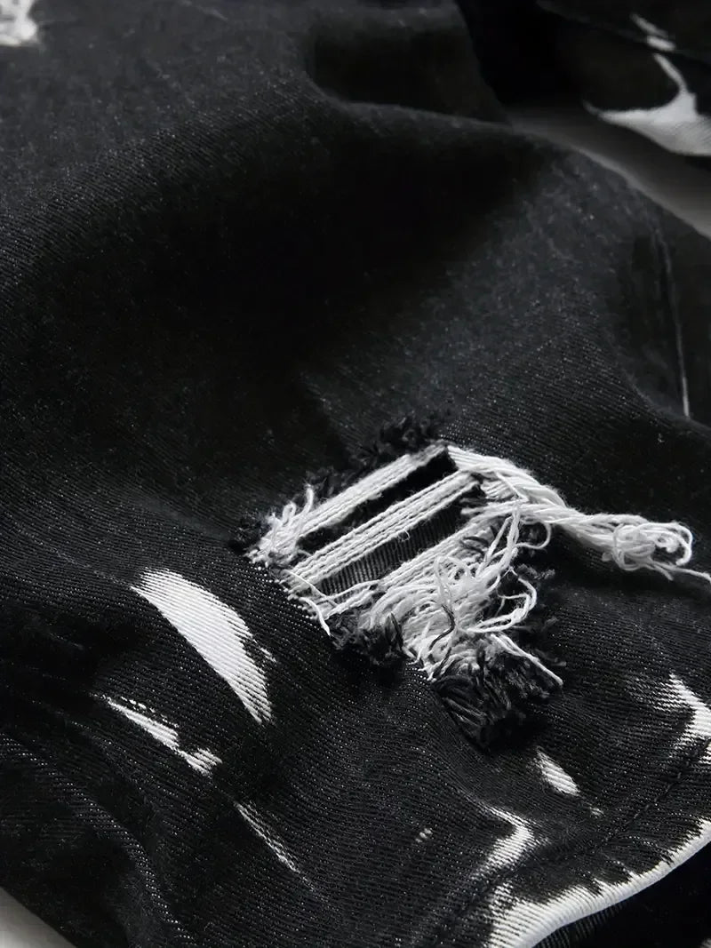 Close-up of a black fabric with frayed edges and white paint splashes.