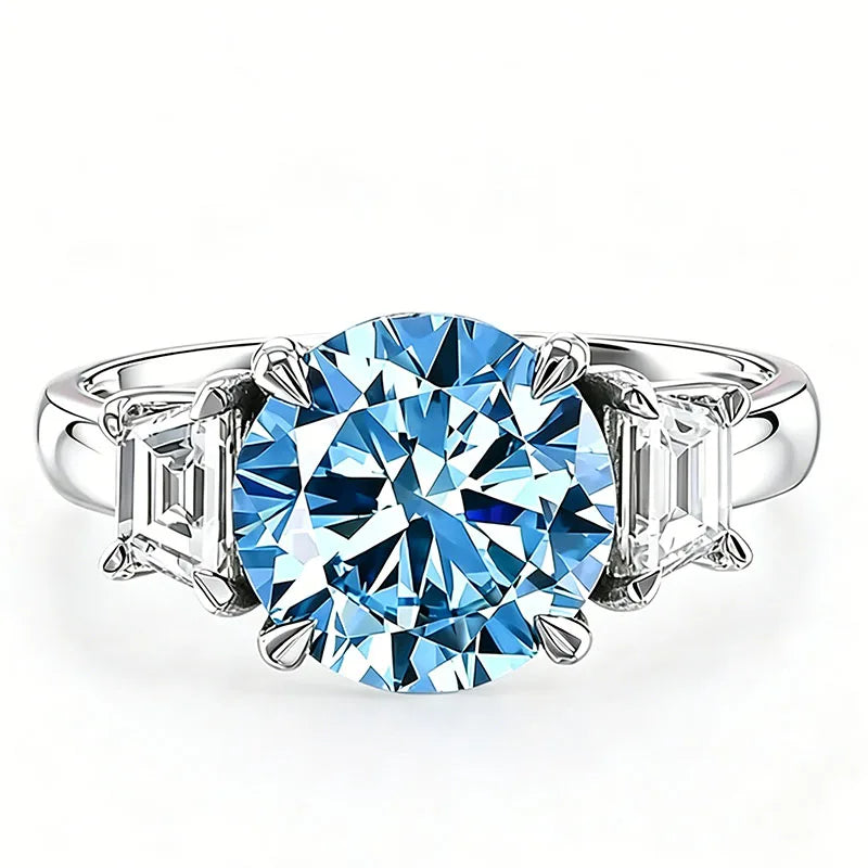 A silver three-stone ring featuring a large round brilliant-cut light blue center gemstone flanked by two baguette-cut side stones, set against a plain white background.