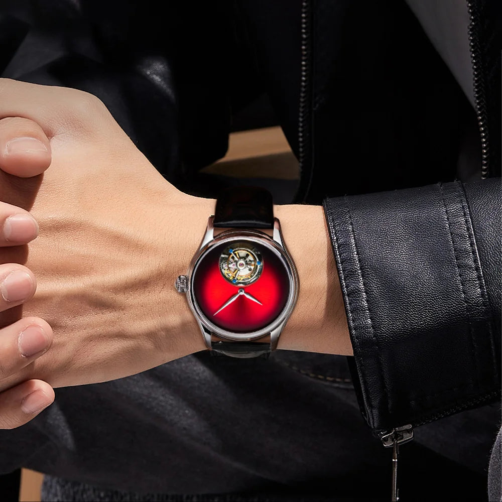 A close-up of a person's wrist wearing a round analog watch with a black leather strap, silver-toned case, and a vibrant red dial featuring a skeletonized center.