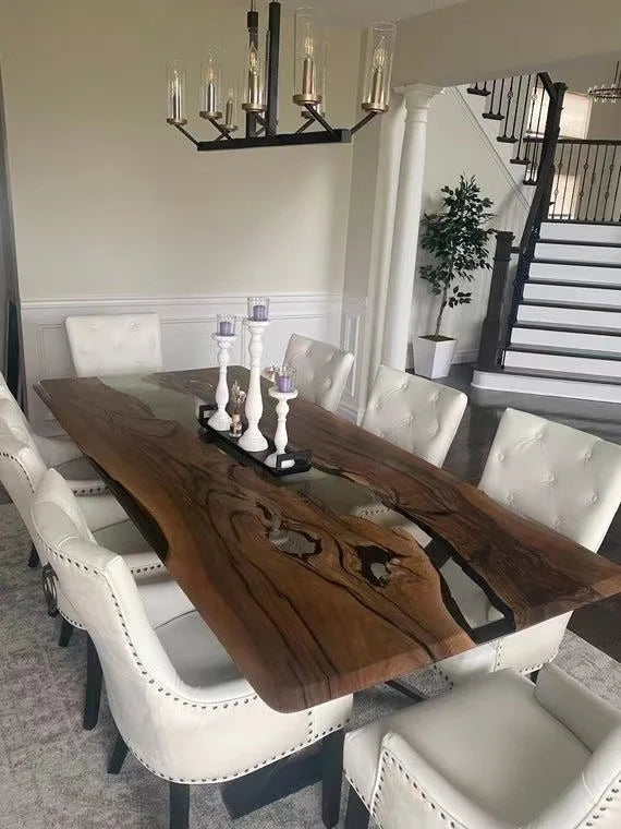 Dining room with a wooden table and white chairs, featuring a staircase in the background.