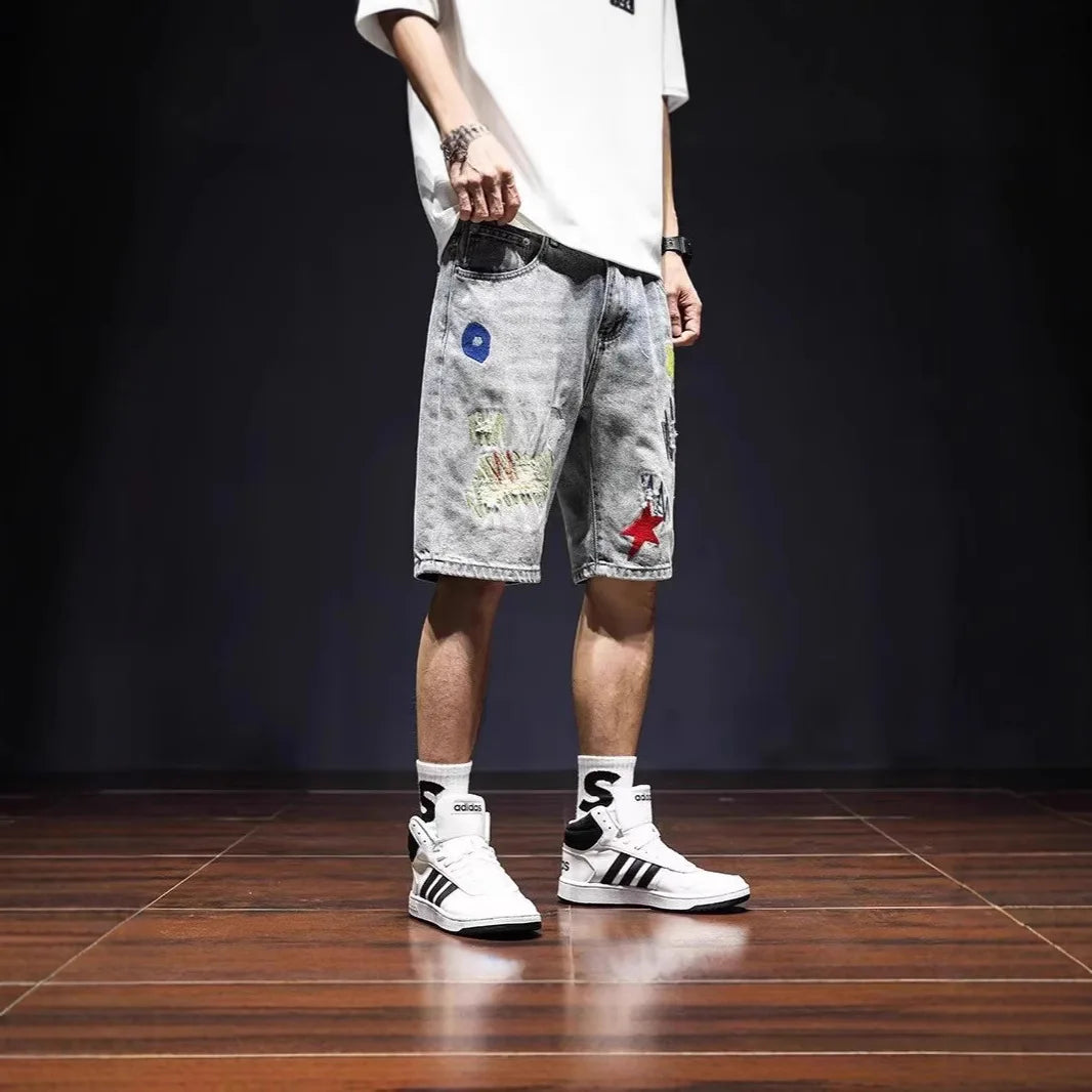 Person wearing a white t-shirt, gray shorts with colorful patches, and white sneakers on a dark floor.