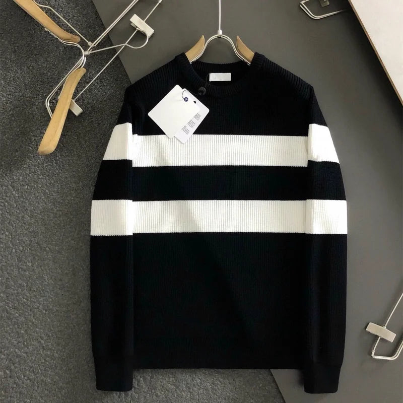 Black and white striped sweater on a hanger against a gray wall.