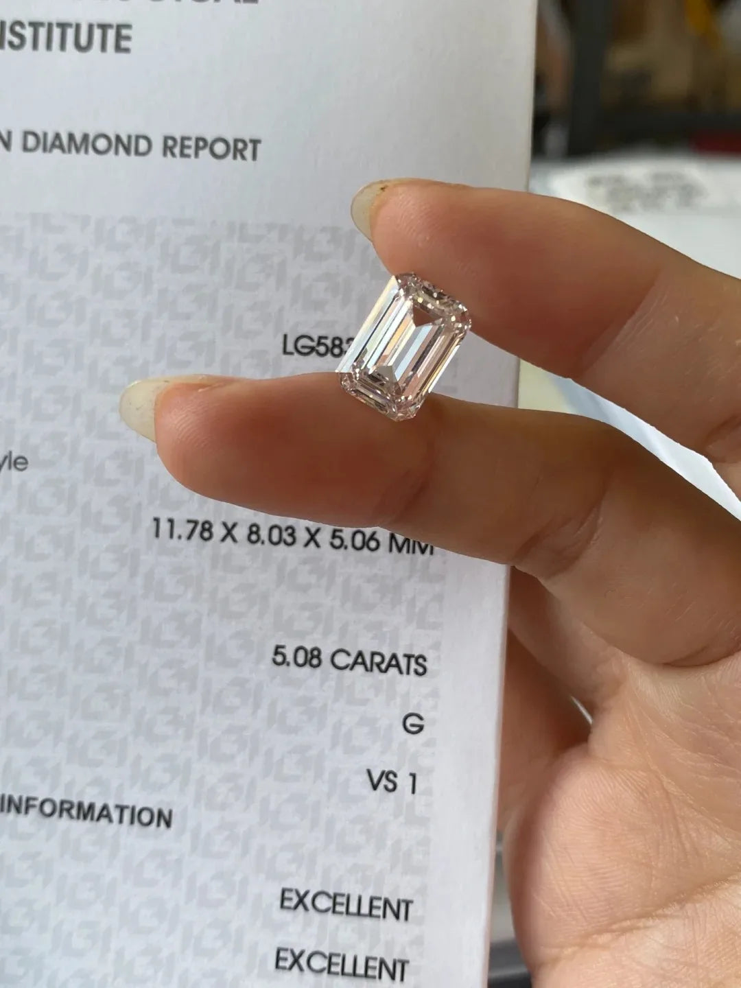 Hand holding a large emerald-cut diamond with a gemological report in the background