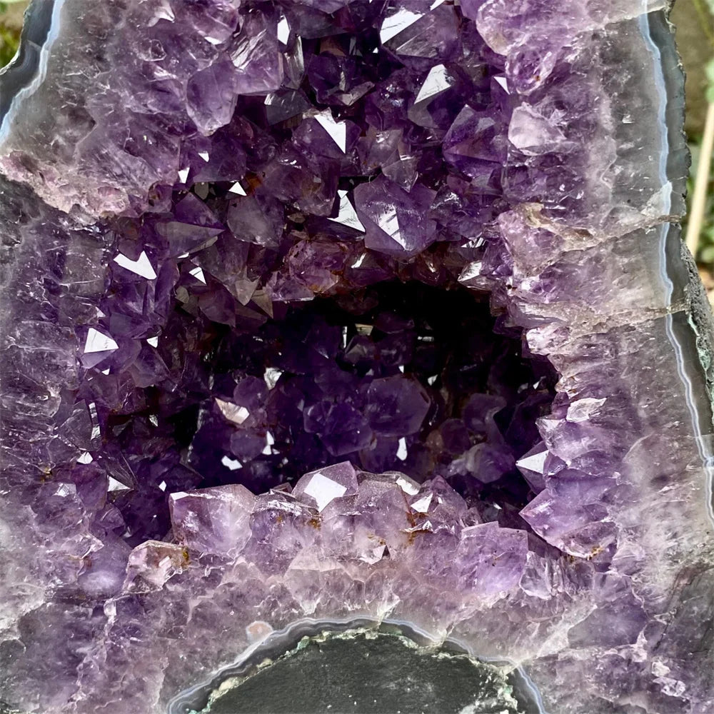 A close-up of an amethyst geode with a hollow center and radiating purple crystal points, showing translucent lavender to deep violet mineral structure against a dark natural matrix.