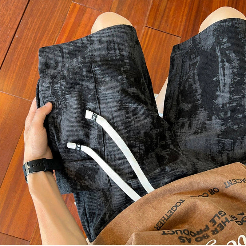 Person wearing black patterned pants with white drawstrings, sitting on a wooden floor.