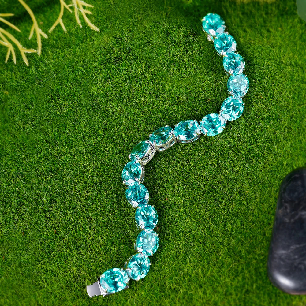 A silver-toned bracelet featuring a curved row of large, faceted turquoise-blue oval gemstones, displayed on a textured green grass-like surface.